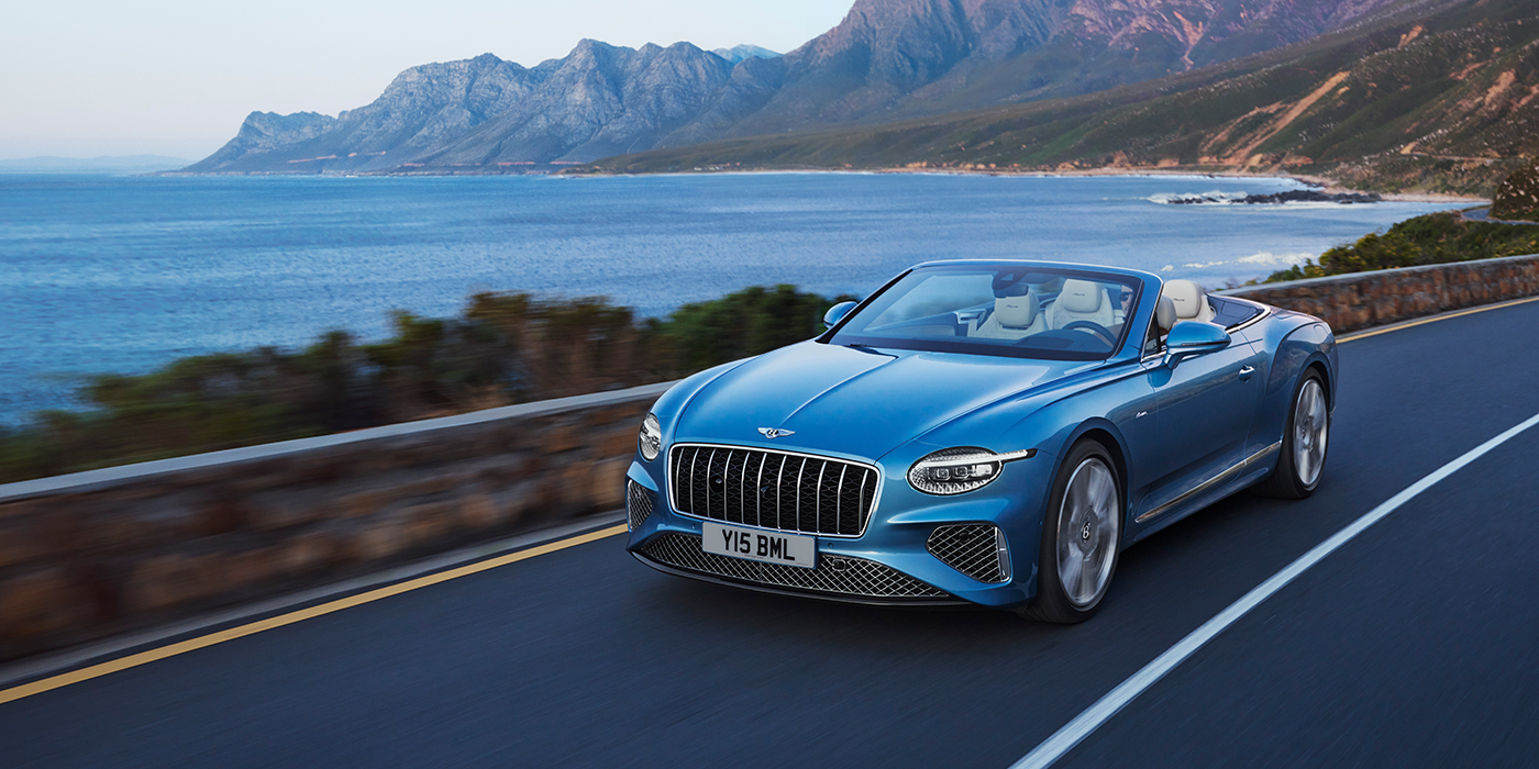 Bentley Mougins New Bentley Continental GTC Azure convertible in Light Windsor blue paint with 22 inch Azure wheels and chrome grill, driving dynamically by the sea