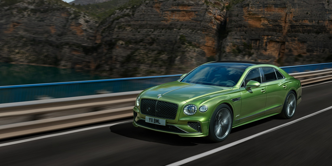 Bentley Mougins Bentley New Flying Spur Speed v8 hybrid sedan driving dynamically on a mountain road in Tourmaline Green paint