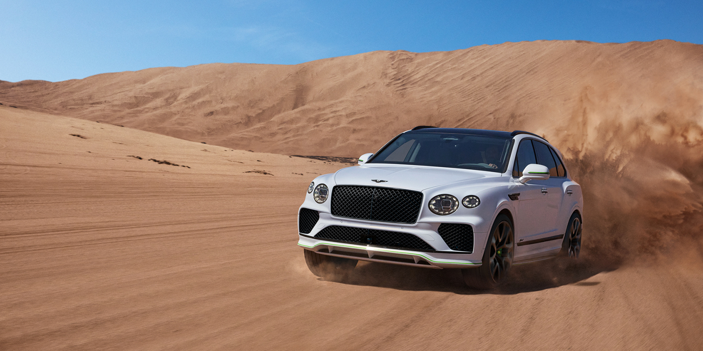 Bentley Mougins Bentley Bentayga Speed SUV front three quarter in Snow Quarts Pearlescent by Mulliner white paint driving dynamically through the desert