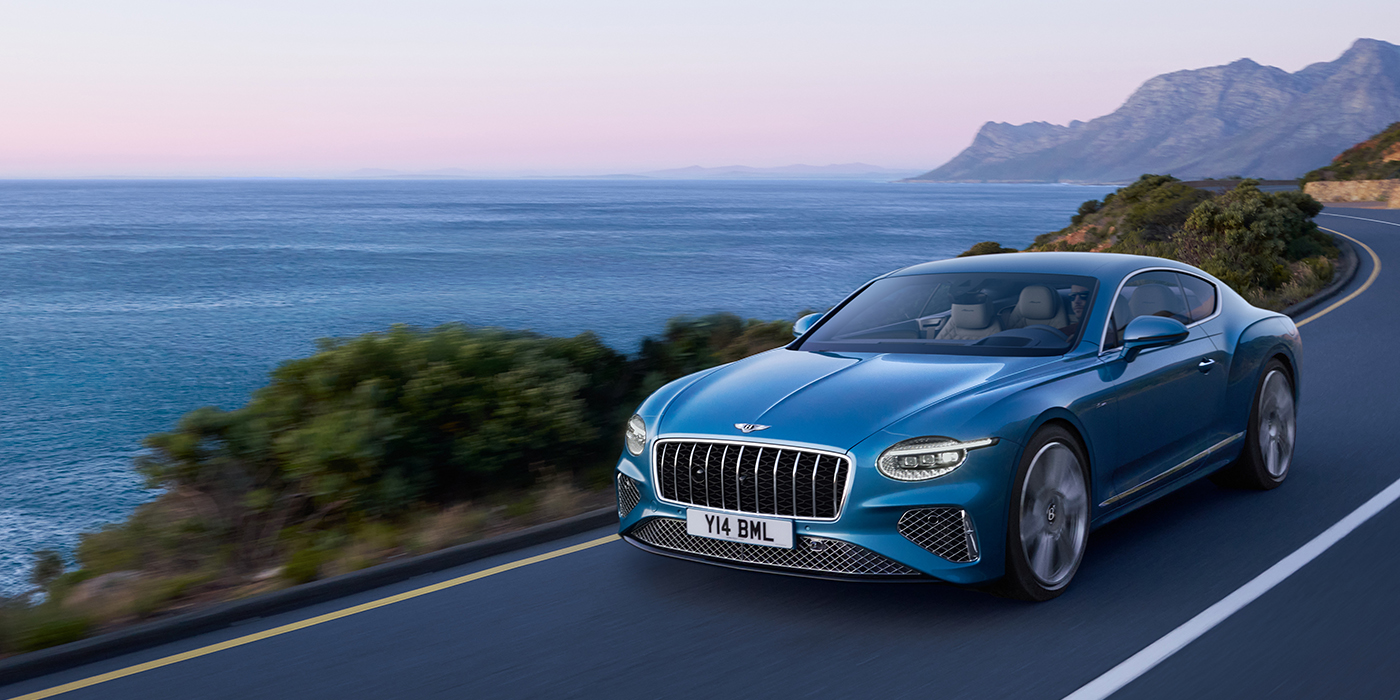 Bentley Mougins New Bentley Continental GT Azure coupe in Light Windsor blue paint with 22 inch Azure wheels and chrome grill, driving dynamically by the sea