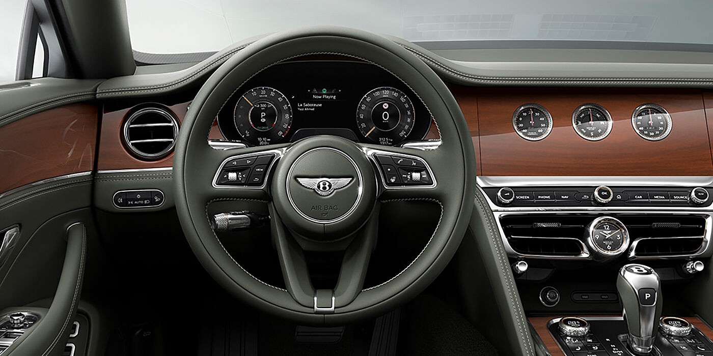 Bentley Mougins New Bentley Flying Spur sedan front cabin in Cumbrian Green hide and Crown Cut walnut veneer showing steering wheel and Rotating Display with three clocks on face