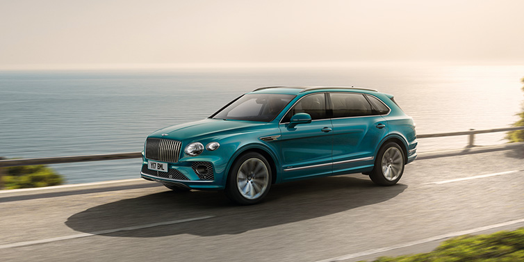 Bentley Mougins Bentley Bentayga Extended Wheelbase Azure SUV in Topaz blue paint driving dynamically by the ocean