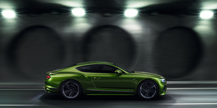 Bentley Mougins Bentley Continental GT Speed coupe profile in Tourmaline Green driving dynamically past a concrete wall at night