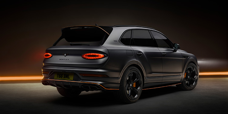 Bentley Mougins Bentley Bentayga S Black Edition SUV rear three quarter in Anthracite Satin paint against a dark red and yellow background