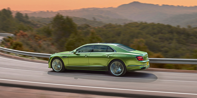 Bentley Mougins Bentley Flying Spur Speed sedan side profile in Tourmaline Green paint driving dynamically on a mountain road at sunset