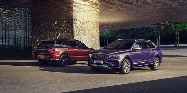 Bentley Mougins A duo of Bentley Bentayga Extended Wheelbase Mulliner SUVs parked in a city environment, with Tanzanite Purple and Cricket Ball red exterior paint