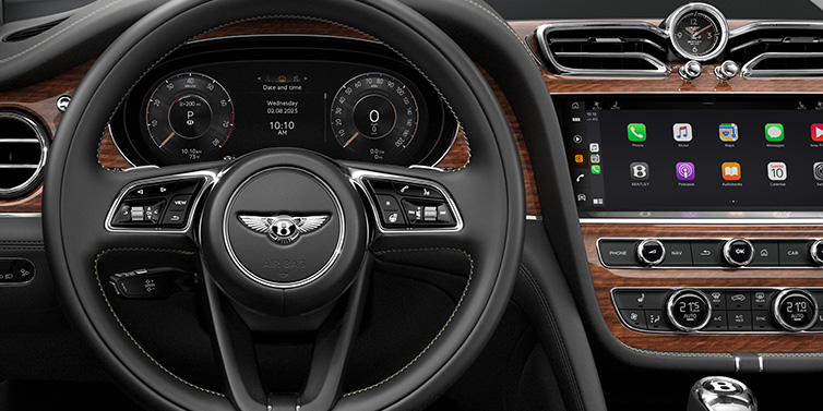 Bentley Mougins Bentley Bentayga SUV front interior detail of steering wheel and driver screens surrounded by Beluga black hide and Crown Cut Walnut veneer